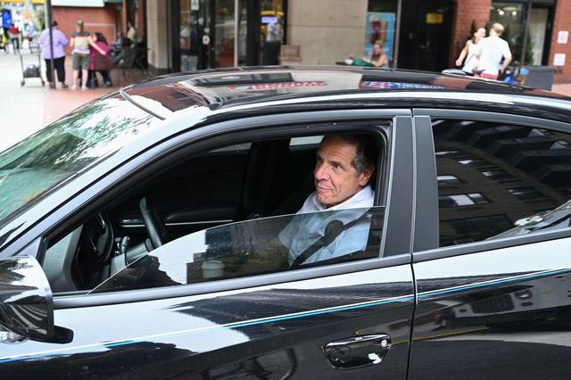 Governor Cuomo wearing a white polo shirt and inside a black car, in the driver's seat